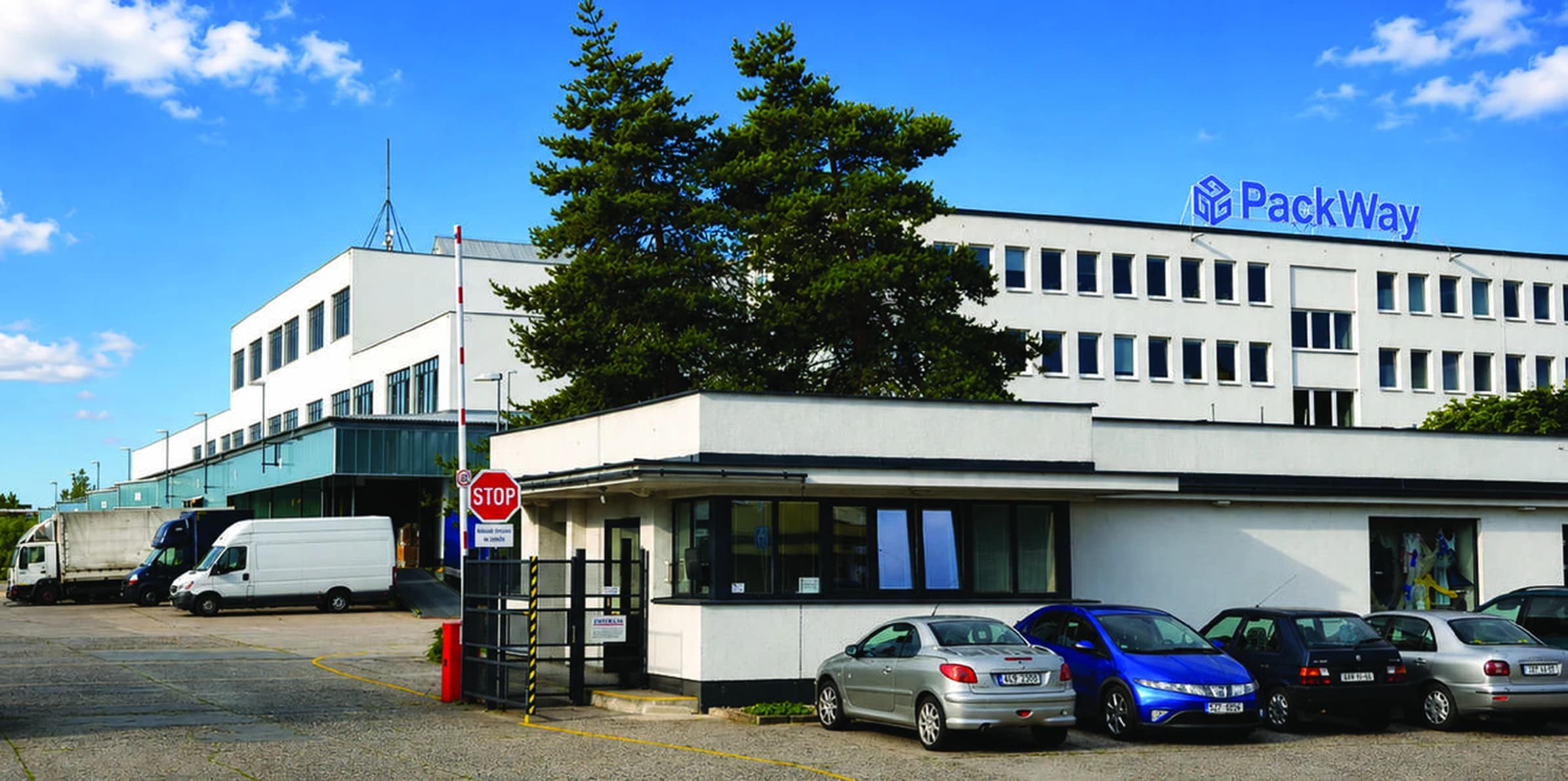 Areál PackWay v Pardubicích, administrativní budova s logem PackWay na střeše, vrátnice se závorou a vozy na parkovišti